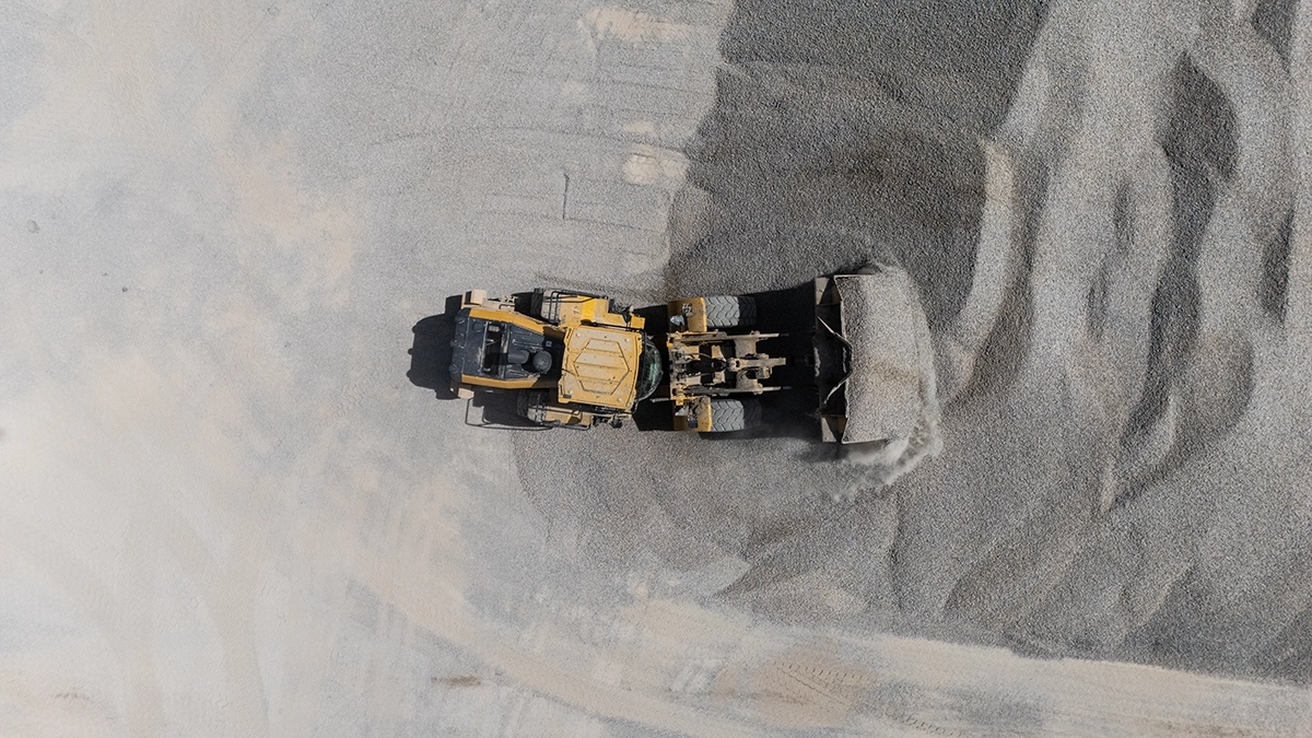 Aerial view of a yellow bulldozer pushing a pile of gravel on a construction or mining site.